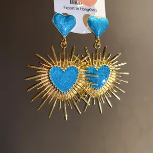 Gros plan de boucles d'oreilles vintage en forme de soleil doré avec des cœurs en émail bleu.