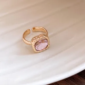 Detail of gold-toned adjustable ring featuring a large square pink gemstone with textured band