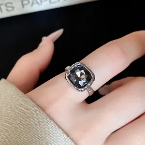 Close-up of a stylish silver-toned ring featuring a square black gemstone on a finger