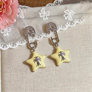 Delicate safety pin star earrings with sparkling zirconia and black cross logo motif detail