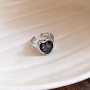 Close-up of a silver heart ring with a dark grey faceted gemstone and an adjustable open band.