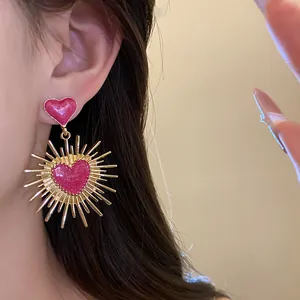 Gros plan de boucles d'oreilles cœur vintage en émail rose avec pendentif soleil doré.