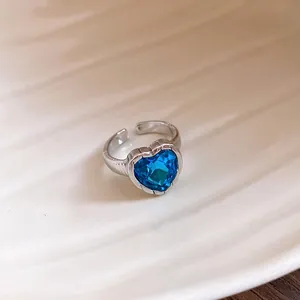 Close-up of elegant silver open ring with a vibrant blue heart-shaped gemstone.