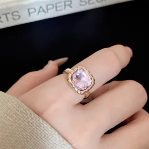 Close-up detail of a gold-toned ring with a radiant square pink gemstone on a finger.