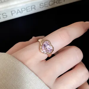 Macro view of pink heart-shaped crystal ring with golden band on finger