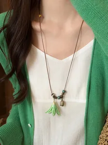 Close-up of ceramic flower pendant necklace with wooden beads on green cardigan