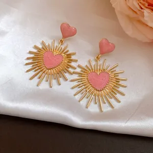 Vue détaillée des boucles d'oreilles vintage avec cœurs roses et rayons d'or.