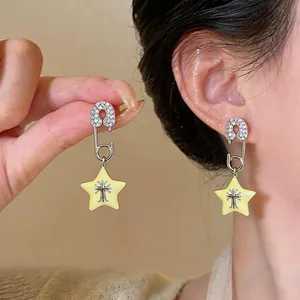 Close-up detail of paperclip star earrings featuring zircon inlay and a cross motif