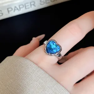 Close-up of elegant silver heart ring with vibrant blue crystal on finger