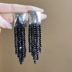 Gros plan de boucles d'oreilles carrées en argent avec longs pompons en perles de verre noires