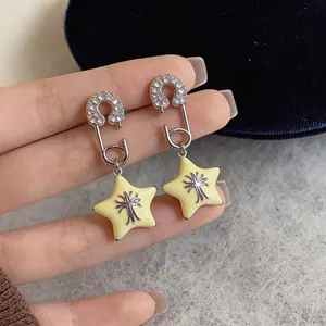 Detailed view of zircon safety pin earrings featuring pale yellow star charms on silver needles