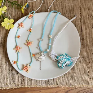 Detail view of handmade summer beaded necklaces with fish and shell charms on a plate.
