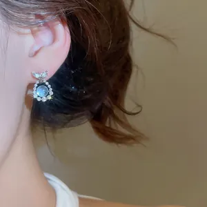 Detailed macro view of sea blue cubic zirconia fish tail stud earrings on a model ear.