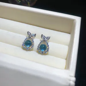 Close-up of sea blue zircon earrings with silver fish tail design in a white jewelry box