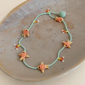 Close-up detail of handmade glass beaded necklace with orange fish charms on a plate