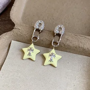 Detailed view of silver safety pin earrings with yellow enamel stars and zircon stones