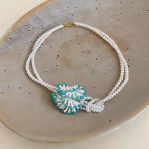 Close-up of a handcrafted white pearl necklace with a turquoise beaded floral detail.
