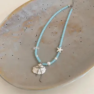 Macro detail of blue glass bead necklace featuring a delicate shell and starfish pendant