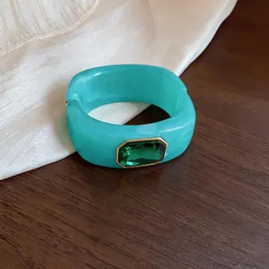 Detailopname van turquoise acryl armband met groen kristal op een houten achtergrond