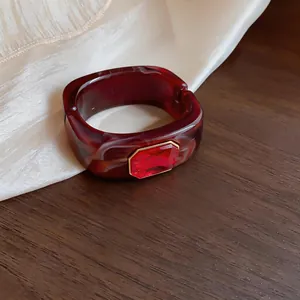 Detail van een donkerrode gemarmerde hars armband met een rode edelsteen in goudkleur.