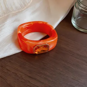 Detailweergave van een oranje gemarmerde hars vierkante armband met amberkleurige steen