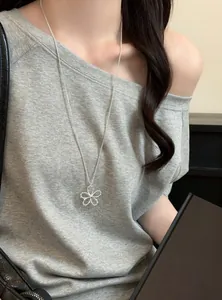 Gros plan d'un collier pendentif fleur argentée porté sur un haut gris à épaules dénudées