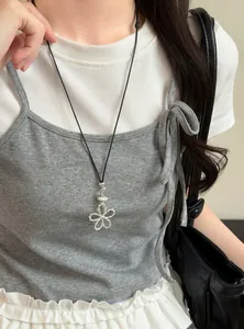 Détail d'un collier pendentif fleur argenté minimaliste porté sur un caraco gris.