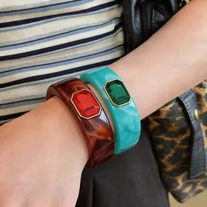 Detailopname van dikke hars armbanden met smaragd geslepen kristallen in amber en blauwgroen.