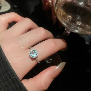 Close-up of light blue zircon halo ring worn on finger in elegant social setting.