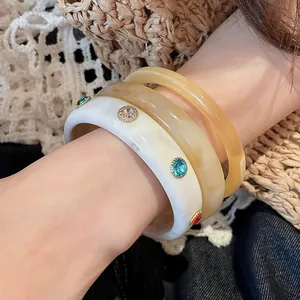 Close-up detail of three stylish resin bangles with colorful crystals on a model's wrist