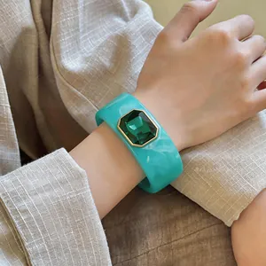 Gedetailleerd overzicht van een turquoise harsarmband met een grote smaragdgroene steen.