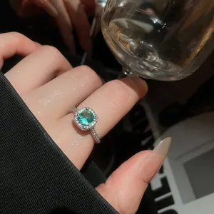 Detailed close-up of an elegant silver ring with green zircon and halo setting on a finger.