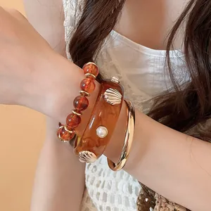 Close-up of amber resin bangle set with shell and pearl details on wrist