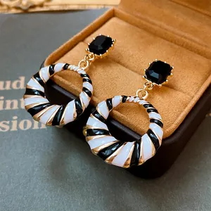 Detail of geometric earrings with black and white striped hoops and black gemstones.