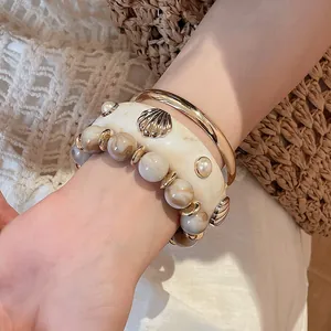 Detailed view of cream resin shell bangle, gold metal ring, and beaded bracelet on wrist