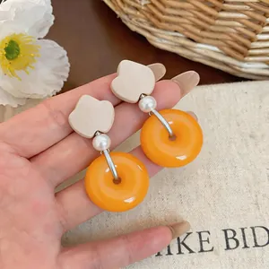 Detailed close-up of orange resin donut earrings with pearl and cream tulip accents