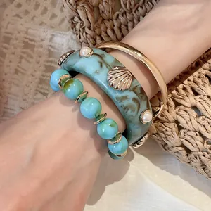 Macro detail of three-piece teal marbled resin and gold metal bracelet set on wrist.