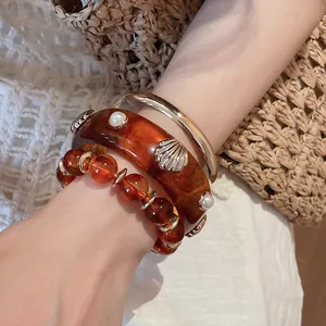 Detail of 3-piece resin bangle set with amber beads, gold-tone metal, and seashell accents.
