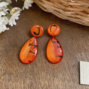 Close-up of French retro orange resin teardrop earrings with black marbled patterns