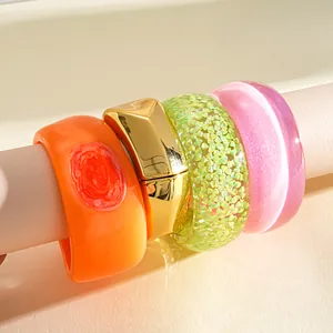 Close-up of chunky geometric resin bangles in vibrant orange, gold, green, and pink.