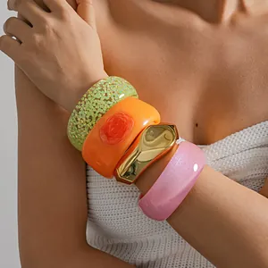 Close-up of stacked colorful resin and metallic geometric bangles on model's arm