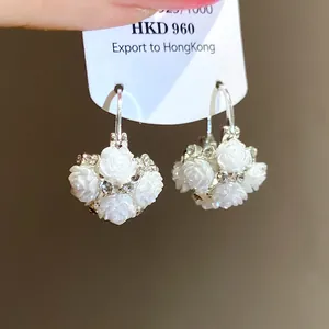 Detailed view of silver needle earrings with white rose flower pendants and rhinestones