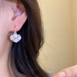 Close-up of white rose flower pendant earrings with delicate crystal accents on ear