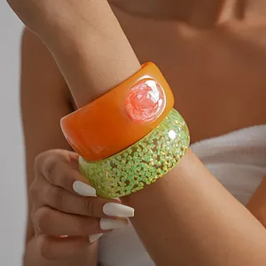 Close-up detail showing vibrant orange and glittery green resin bangles on a model's wrist
