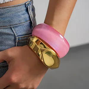 Close-up detail of oversized pink glitter resin and golden geometric statement bangles on wrist