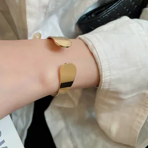 Close-up view of a minimalist irregular gold metal open cuff bracelet on wrist.