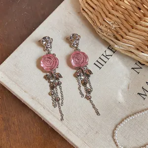 Primo piano di eleganti orecchini a rosa in resina rosa con delicate nappe a catena argento