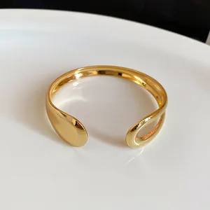 Macro view of a minimalist irregular gold metal open cuff bracelet with polished finish
