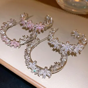 Detailed macro view of elegant C-shaped earrings with sparkling zircon flower motifs.