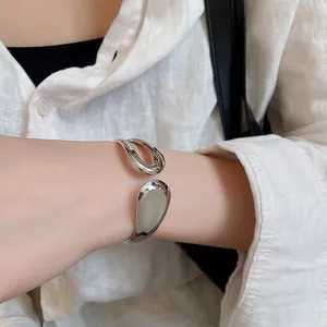 Close-up of a minimalist irregular silver metal open cuff bracelet worn on wrist